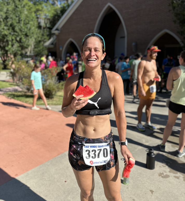 A runner after a race smiling while eating watermelon.